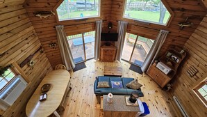 Una cabaña acogedora con interior de madera, un comedor, una zona de estar con una mesa de café y ventanas amplias con vistas al jardín trasero.