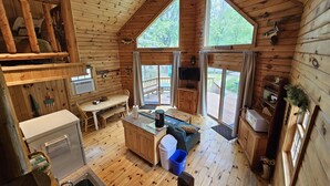 Interior de una cabaña con detalles de madera, un comedor, una cocina y un amplio ventanal con vistas a una terraza.