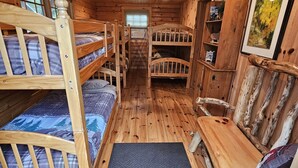 Interior de cabaña con literas de madera, una escalera central y una decoración rústica.