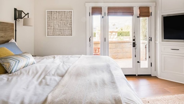 Ein Schlafzimmer mit einem Bett, einem Fernseher, einer zur Außenseite führenden Tür und einer Wandlampe.