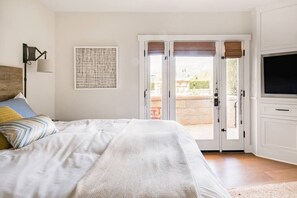 A bedroom with a bed, a television, a door leading outside, and a wall-mounted lamp.