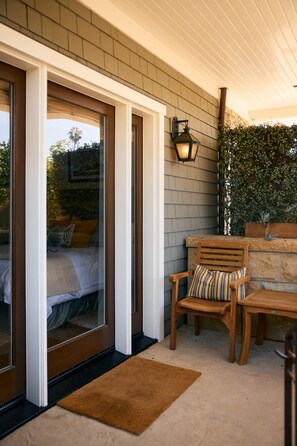 A room with a sliding glass door leading to a bed, a wooden chair with a striped cushion, and a stone wall with a lantern.
