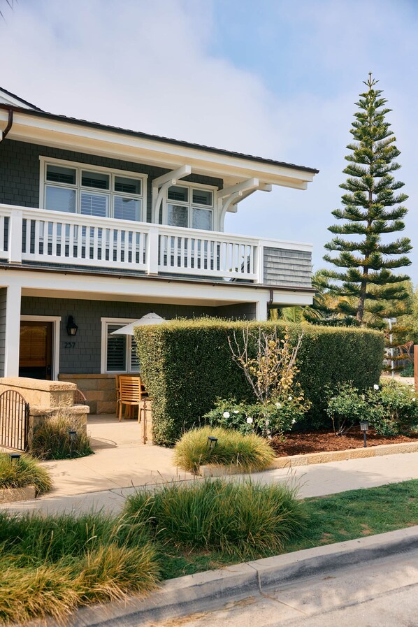 A two-story house with a balcony, a well-maintained lawn, and a tall pine tree.