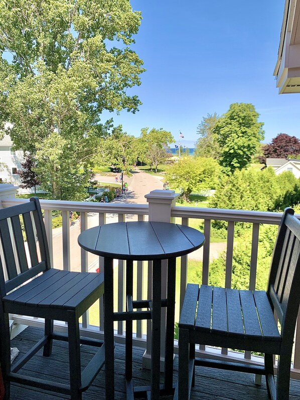 A balcony with two wooden chairs and a small round table, overlooking a residential street with houses and trees.