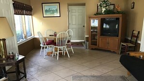 A living room with a dining table, white chairs, a sofa, a television, and a cabinet. - Three Bedroom House on Private Lake Delancy in Ocala National Forest (Salt Springs)