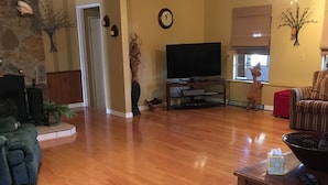 A spacious living room with hardwood flooring, a television, a fireplace, and a stone accent wall. - Three Bedroom House on Private Lake Delancy in Ocala National Forest (Salt Springs)
