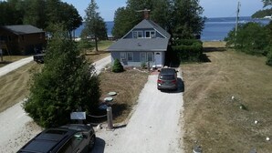 Een twee verdiepingen tellend huis met een grindpad dat leidt naar een voordeur, omringd door bomen en met uitzicht op de zee.