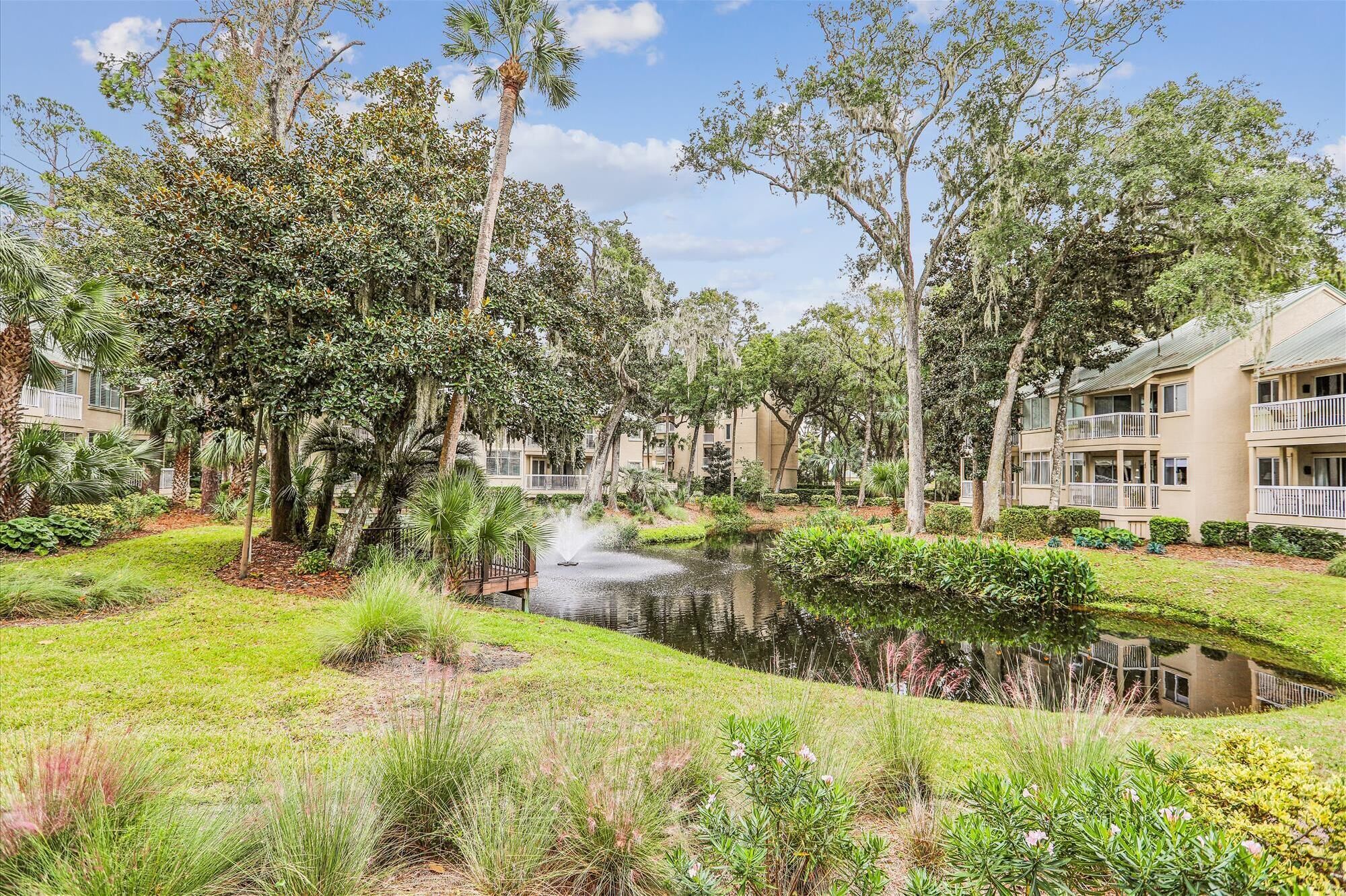 A landscaped garden with a pond, surrounded by mature trees and a building with balconies.