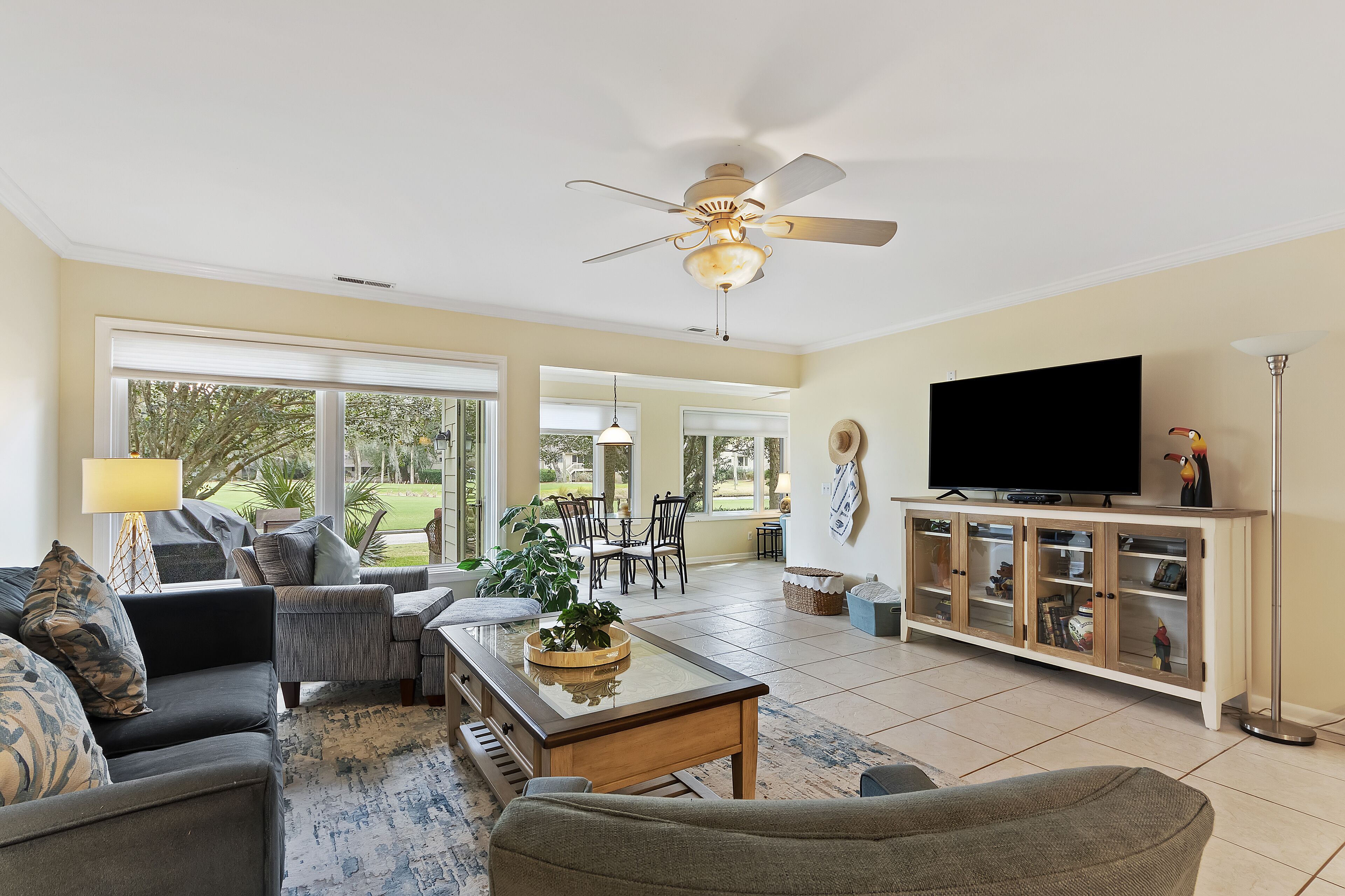 A spacious living room with a ceiling fan, a large TV, and a dining area with a table and chairs.