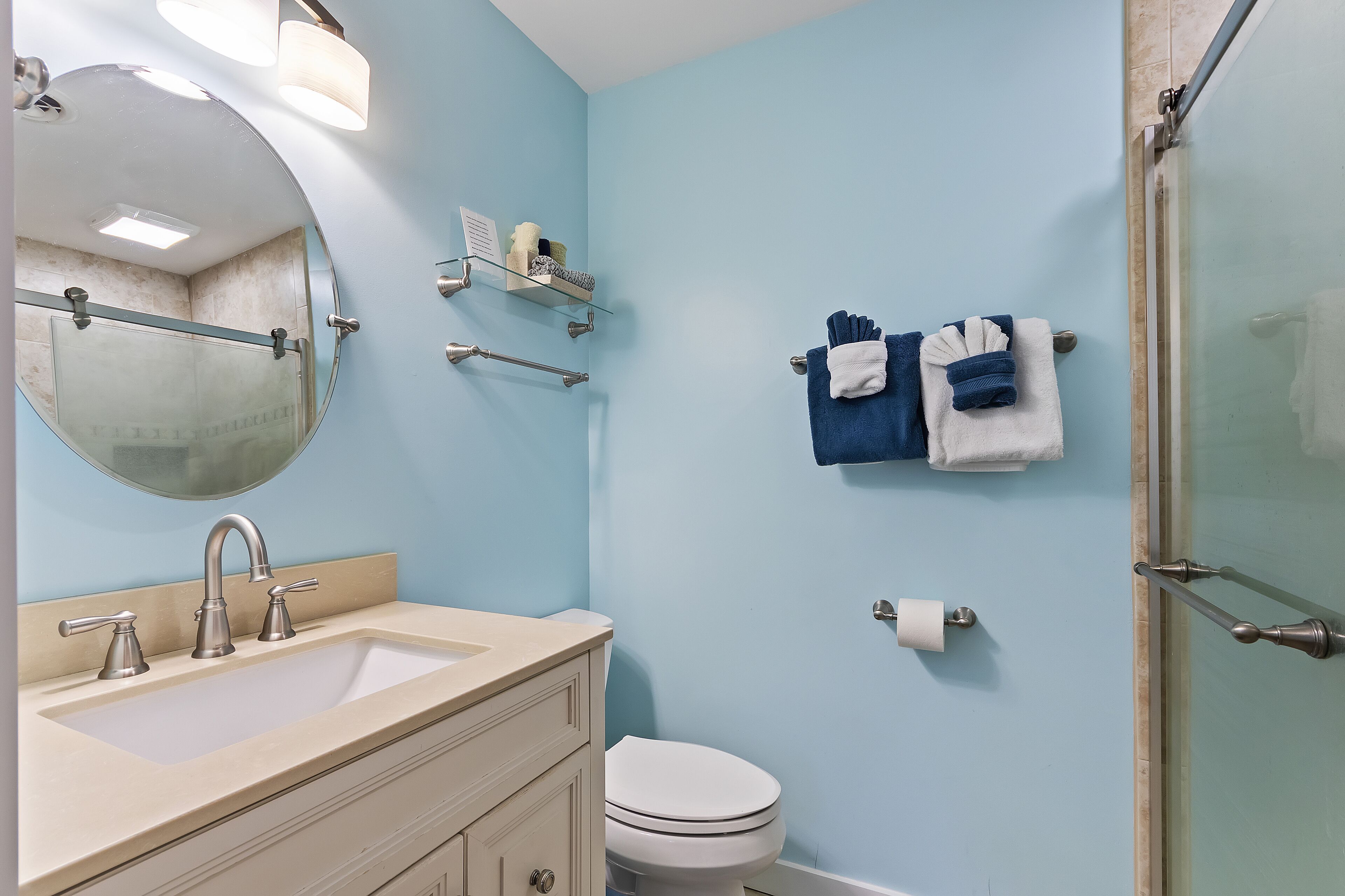 Un bagno con lavandino, specchio, portasciuga e box doccia in vetro.