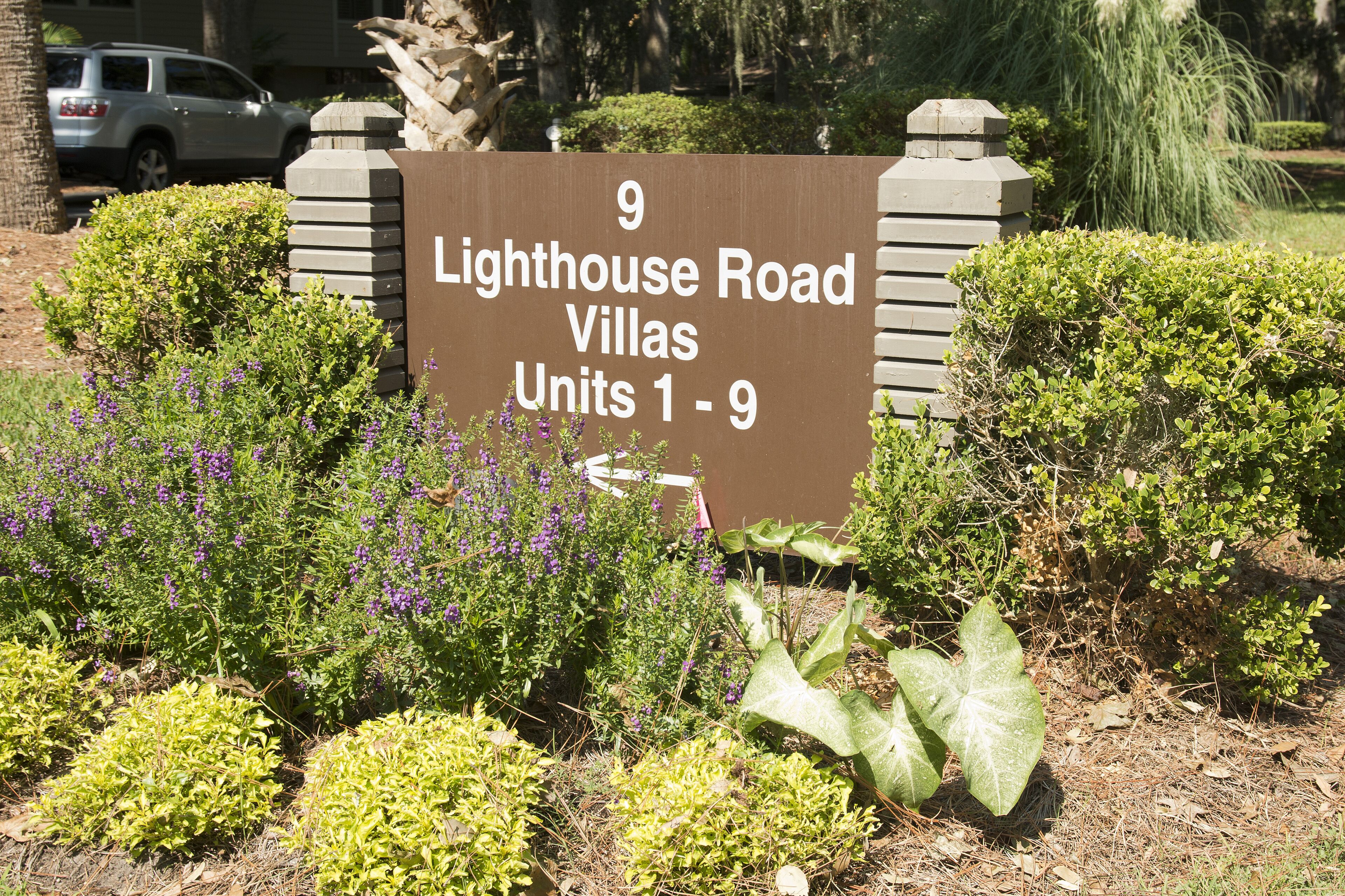 Une enseigne indiquant « Lighthouse Road Villas, logements 1 à 9 », entourée de verdure et avec une voiture garée à proximité.