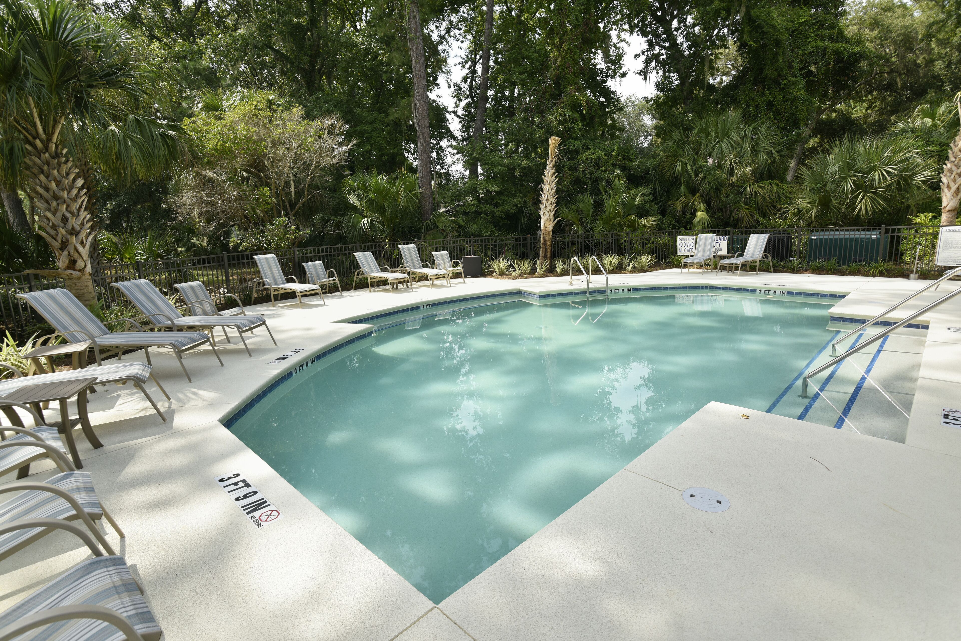 A pool with lounge chairs and a sign indicating a shallow water depth of 3 feet.