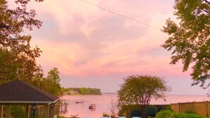 A backyard with a swimming pool, lounge chairs, a gazebo, and a view of a lake at sunset.
