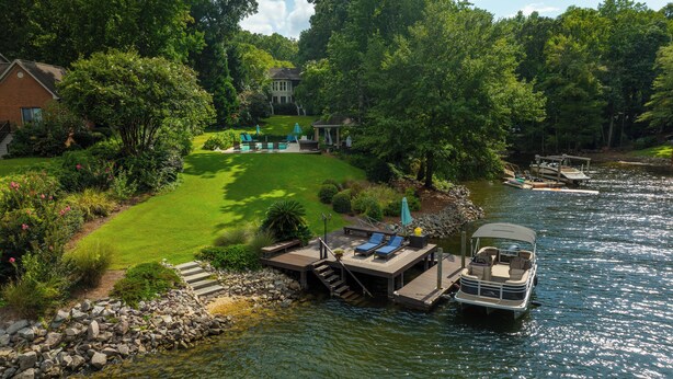 A lakeside property with a dock, a grassy lawn, and a house in the background.