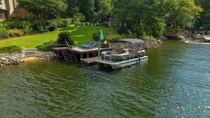 A houseboat docked at a private dock with a small deck, a covered seating area, and a lounge chair.