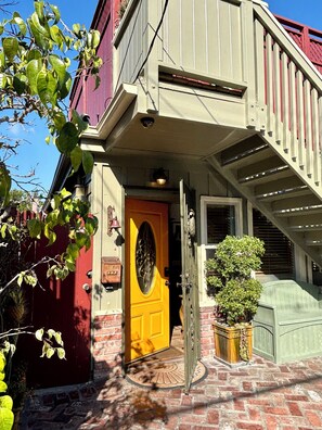 Un bâtiment à deux étages avec une porte jaune, une entrée en briques et une petite plante en pot.