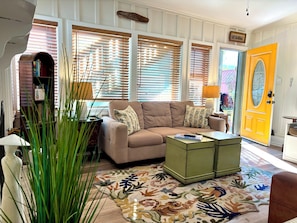 A living room with a beige sofa, a green coffee table, a floral rug, and a yellow door.