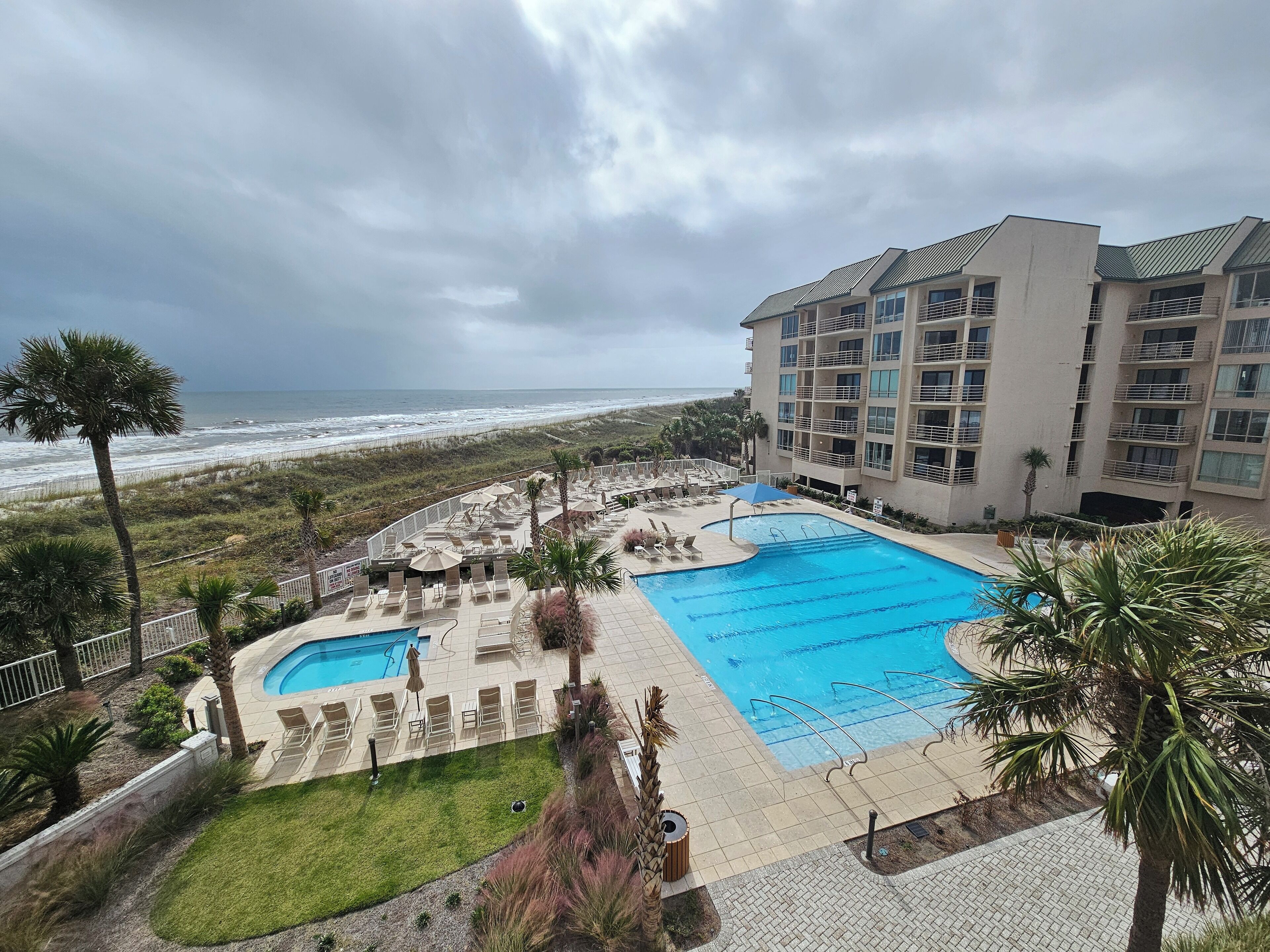 A hotel with a pool area, including a main pool and a smaller pool, surrounded by lounge chairs and umbrellas.