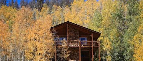 A cabin with a stone foundation, wooden exterior, and a balcony.