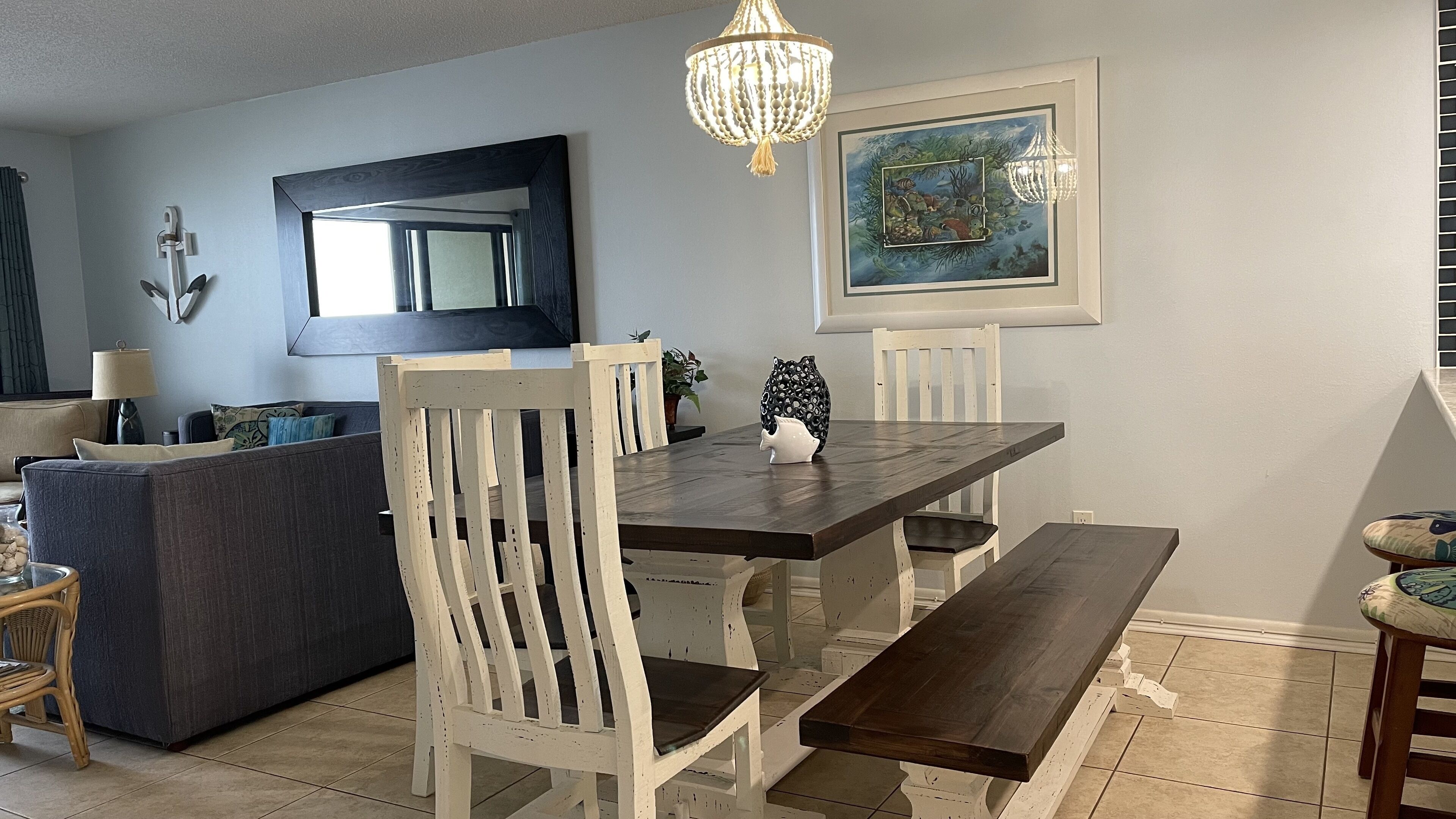 A dining area with a wooden table, white chairs, a bench, a chandelier, and a framed painting on the wall.