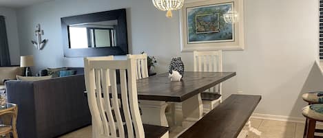 A dining area with a wooden table, white chairs, a bench, a chandelier, and a framed painting on the wall.