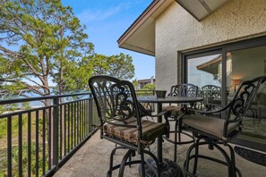 A balcony with outdoor furniture, including two chairs and a table, overlooking a body of water and trees. - 5th Floor Penthouse w/ Amazing Water Views (Hilton Head Island)