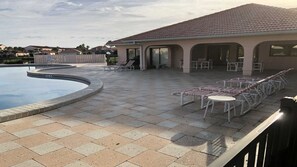 A swimming pool with a tiled deck, lounge chairs, and a covered patio area.