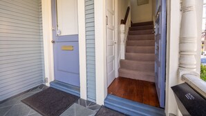 Una entrada principal con una puerta azul, una escalera de madera y un felpudo de piedra.