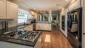 A modern kitchen with white cabinetry, a central island with a gas stove, stainless steel appliances, and a view into the adjacent dining area. - Walla Walla Gem - Peaceful, Private and a Perfect Central Location  (Walla Walla)