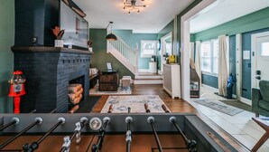Una sala de estar moderna con chimenea, mesa de fútbol y una escalera que sube a otro nivel.