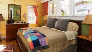 A bedroom with a wooden bed, a colorful quilt, a dresser, a mirror, and a window with curtains. - Fabulous Downtown Living (Santa Barbara)