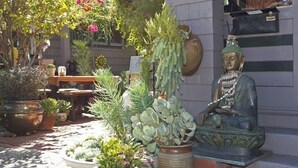 A statue of a seated figure in a garden setting with various potted plants and a small table. - Fabulous Downtown Living (Santa Barbara)