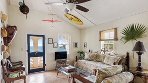 Un salon comprenant un canapé, un téléviseur, un ventilateur de plafond et une porte donnant sur un balcon.