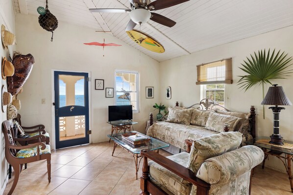A living room with a sofa, a television, a ceiling fan, and a door leading to a balcony.