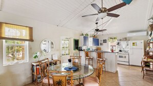 Une cuisine spacieuse avec un coin repas, comprenant une table à plateau en verre, des chaises en bois et un ventilateur de plafond.