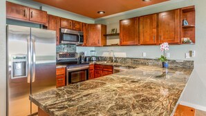 A kitchen with wooden cabinets, stainless steel appliances, and a granite countertop. - Eastside Zen Retreat, Pono Kai
4/25-5/3 - Discounted 15% (Kapa'a)