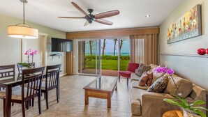 A spacious living area with a ceiling fan, a dining table with chairs, a sofa with cushions, and a large window offering a view of the outdoors. - Eastside Zen Retreat, Pono Kai
4/25-5/3 - Discounted 15% (Kapa'a)