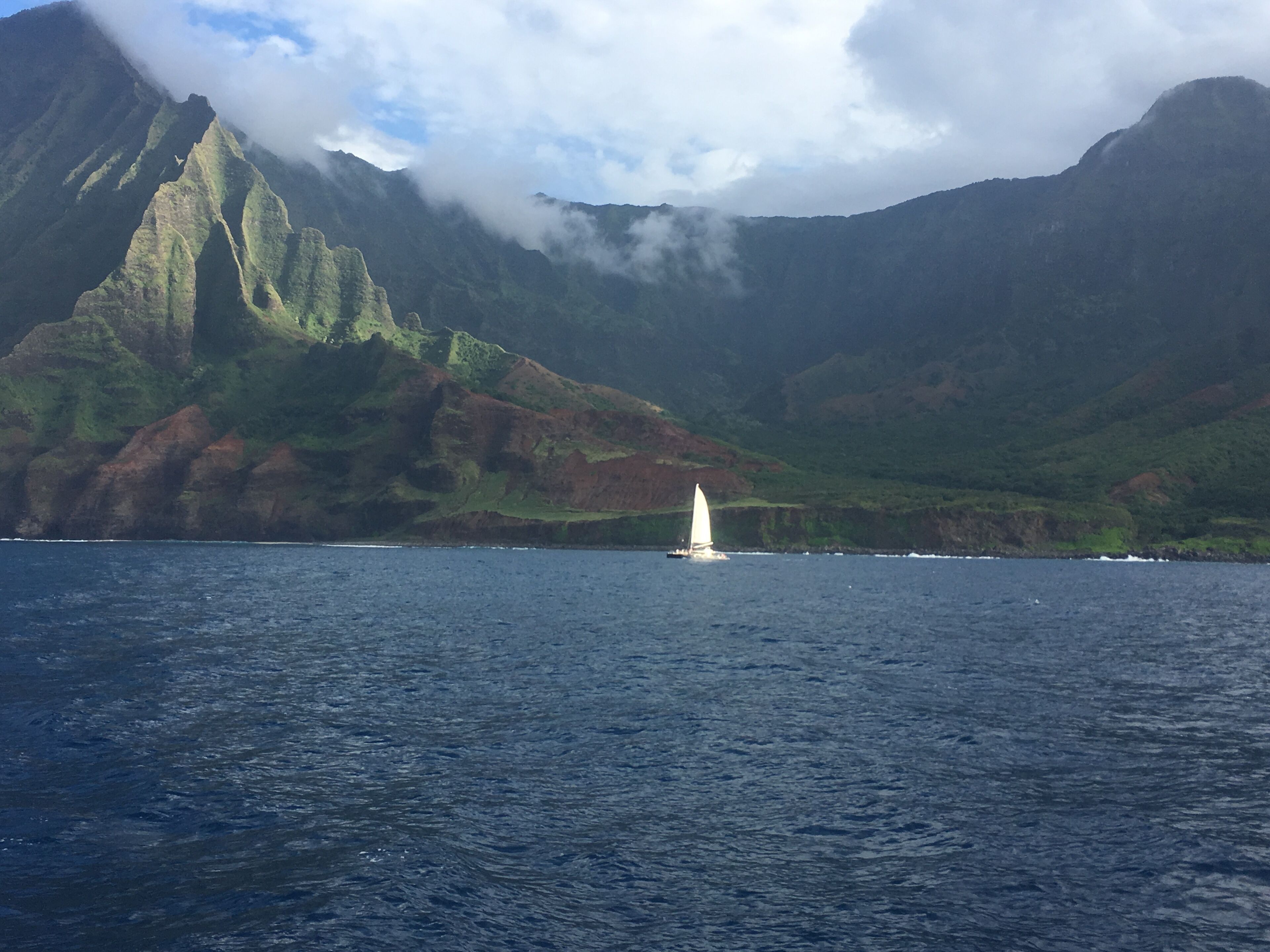 A sailboat on a calm sea with a mountainous backdrop.