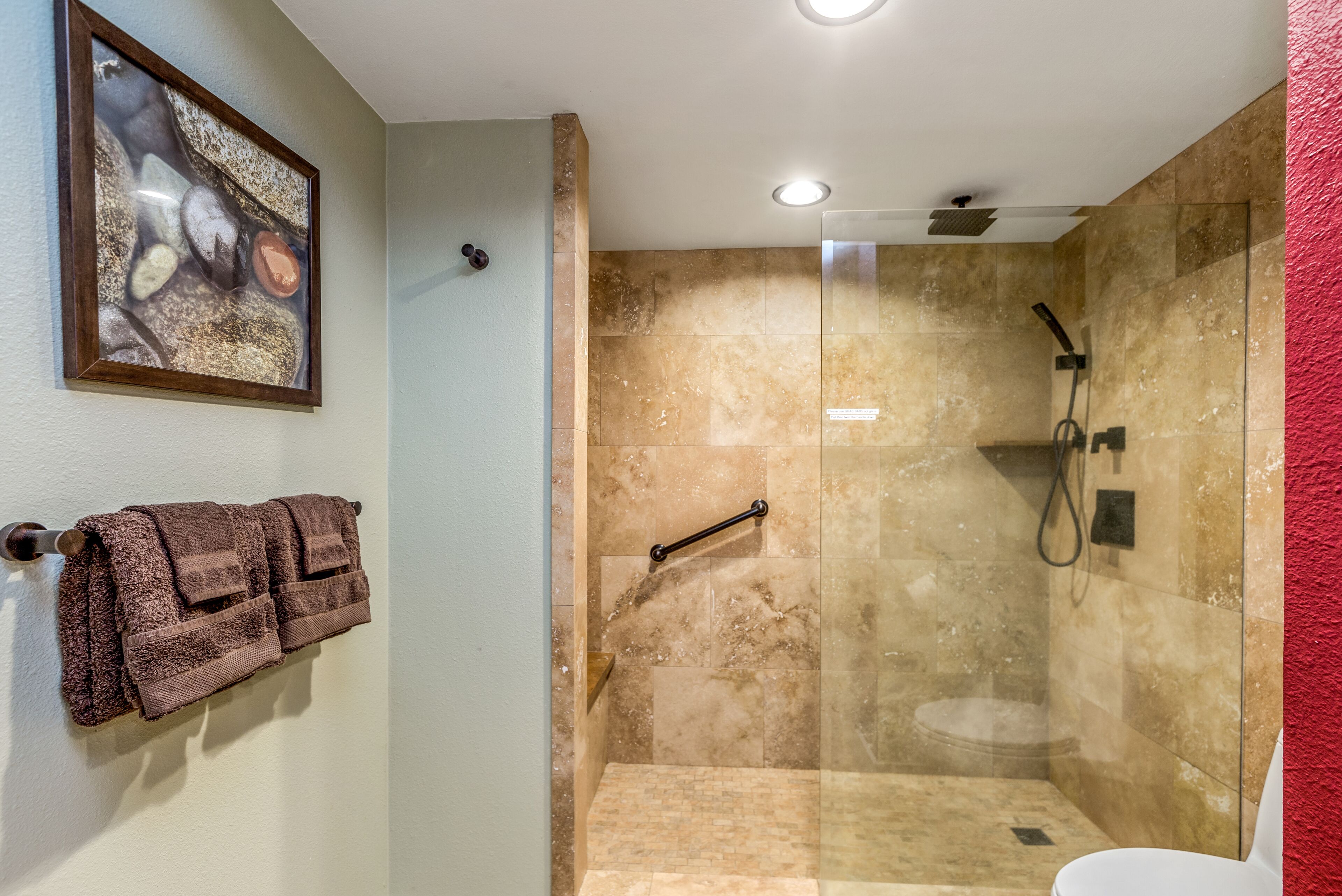 Ein Badezimmer mit einer gläsernen Duschkabine, einem Handtuchhalter mit braunen Handtüchern und einem gerahmten Bild an der Wand.