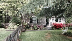 Een huis met voortuin, houten schutting en tuin met verschillende planten en bloemen.
