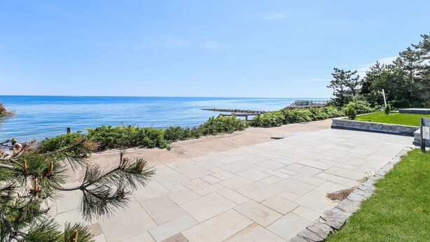 A patio area with a view of the ocean, a stone pathway, and a grassy area with trees. - Ocean Front, Private Beach, Ocean View , Private patio (Dennis)