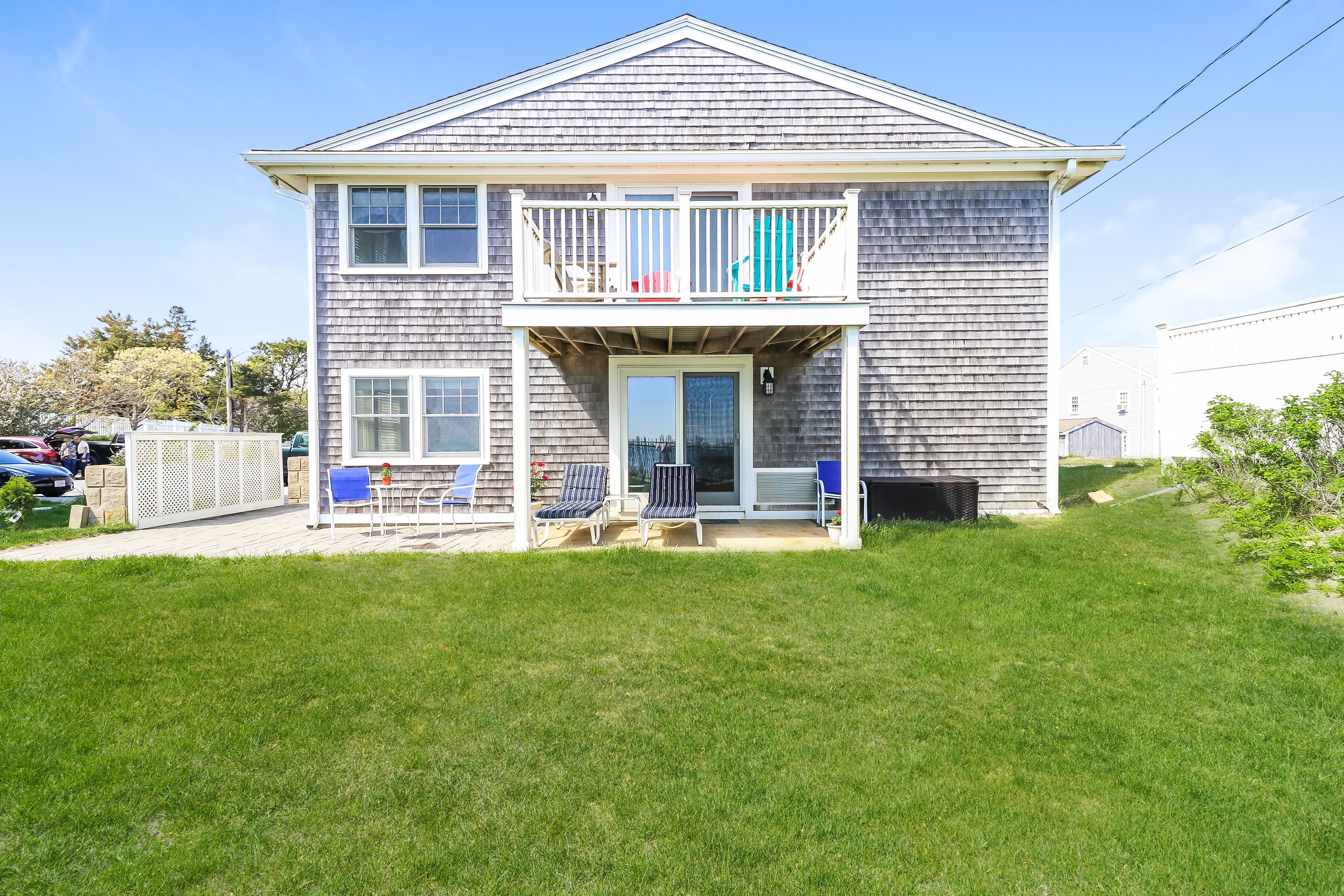 A two-story house with a balcony, a front door, and a small porch area with chairs.