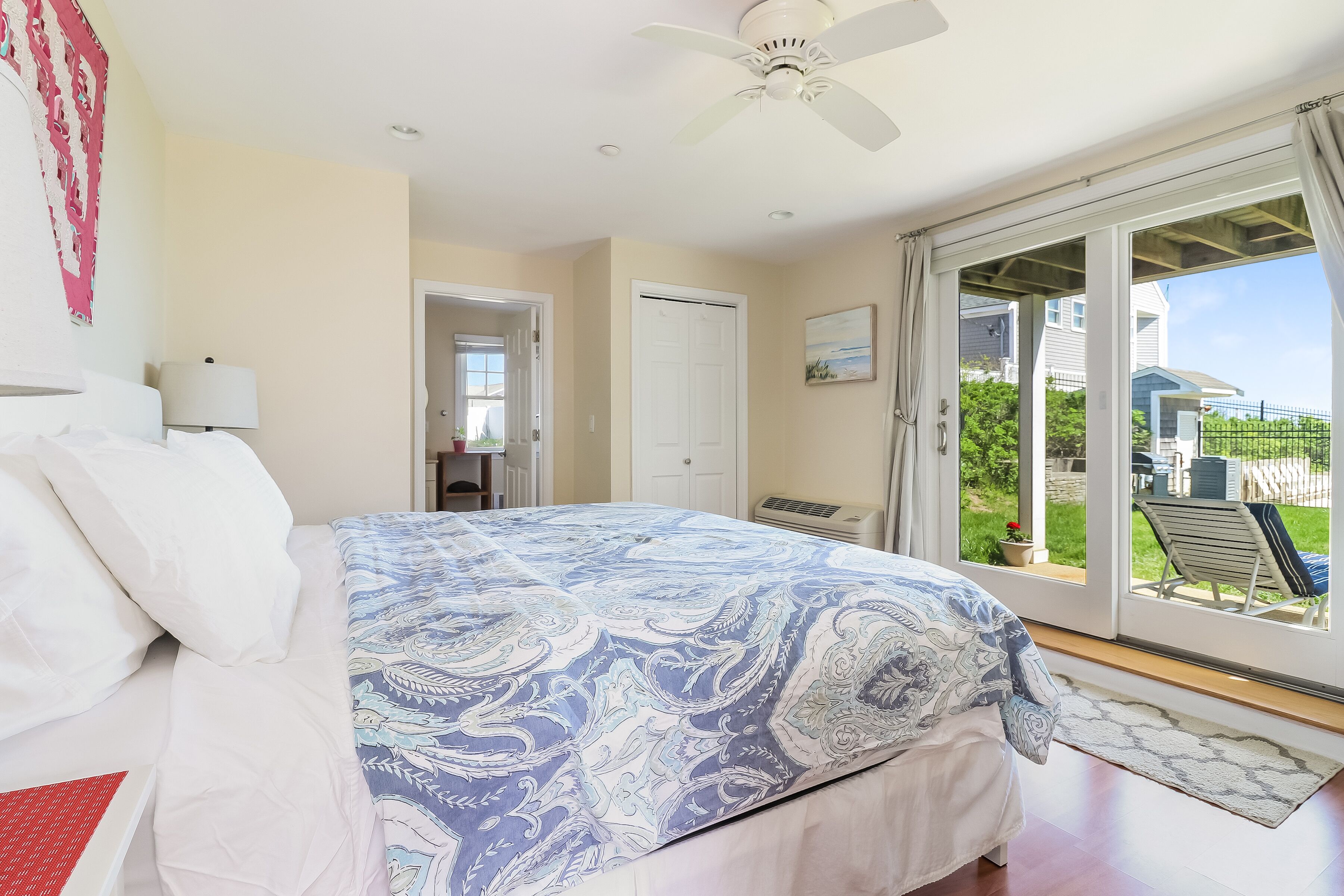 A bedroom with a bed, a ceiling fan, a sliding glass door to the outside, and a view of the backyard.