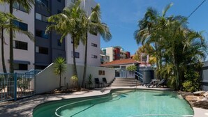 Una piscina de diseño curvo, rodeada de palmeras y un edificio con varios balcones.