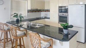 Una cocina moderna con una isla central, electrodomésticos de acero inoxidable y un comedor con sillas de mimbre.