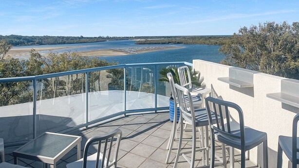 Una terraza con balaustrada de vidrio que da a un río y una playa.