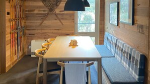 L’intérieur d’un chalet en bois, avec une table à manger, un banc, des skis et des tableaux encadrés accrochés aux murs.