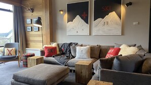 Un salon moderne comprenant un canapé, un pouf et une table basse, et agrémenté d’une décoration et d’œuvres d’art sur le thème du ski.