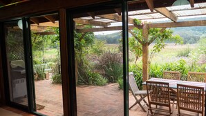 A patio area with a table and chairs, a grill, and a view of a garden and hills. - Back Forest Retreat Sunrise Cottage (Back Forest)
