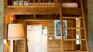 A wooden interior with a loft bed, a ladder, and a floor lamp. - Back Forest Retreat Sunrise Cottage (Back Forest)